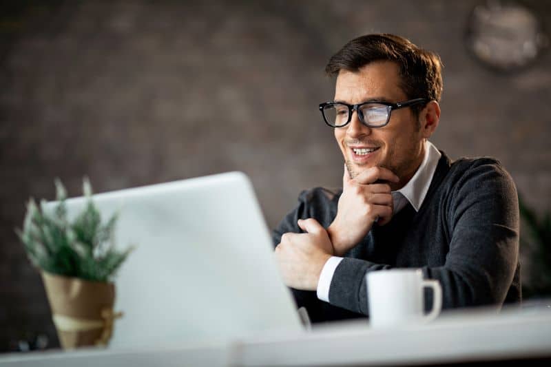 Homem satisfeito com seu sistema de cobrança automatizado sorri enquanto utiliza notebook.