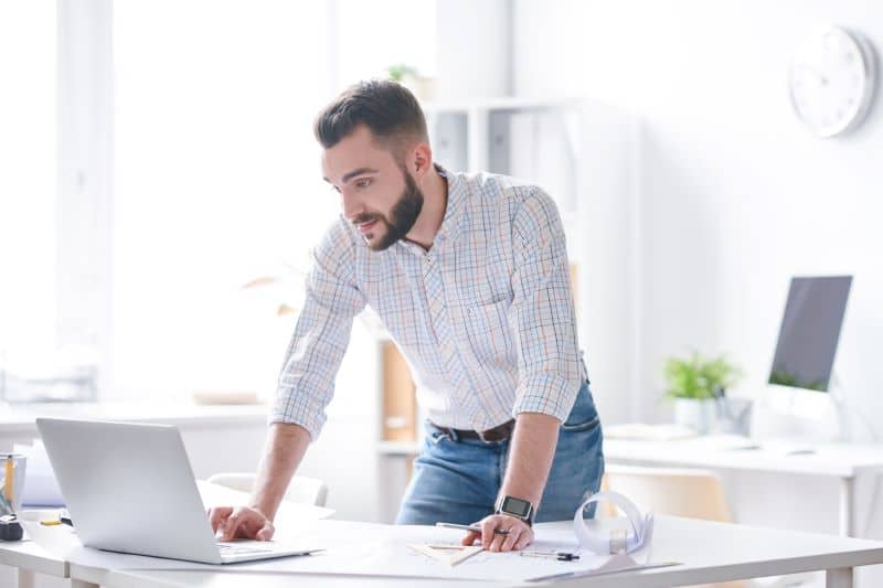 Programador em pé curvado sobre a mesa calculando a regra dos 40 no escritório de sua empresa.