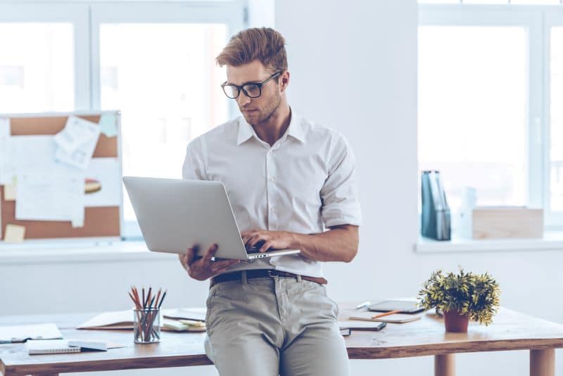 Homem recostado na mesa com notebook em mãos verificando o melhor modelo de receita para sua agência.