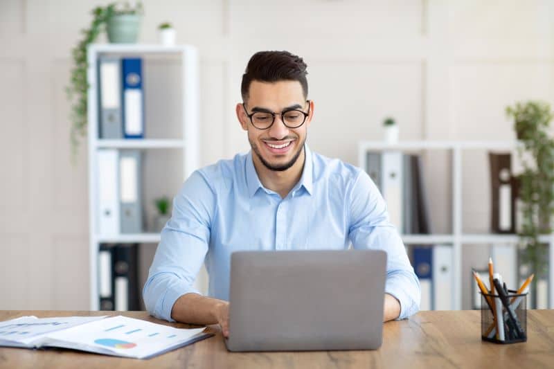 Homem sorridente em escritório realizando a gestão do plano de contas contábil via software em seu computador.