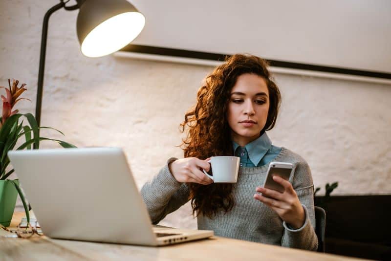 mulher no escritório tomando café enquanto lê mensagem de reajuste de preço para clientes