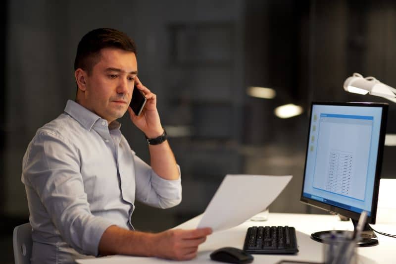 Tabela de precificação: homem trabalhando no escritório e falando ao celular com expressão séria, com tela do computador à mostra.