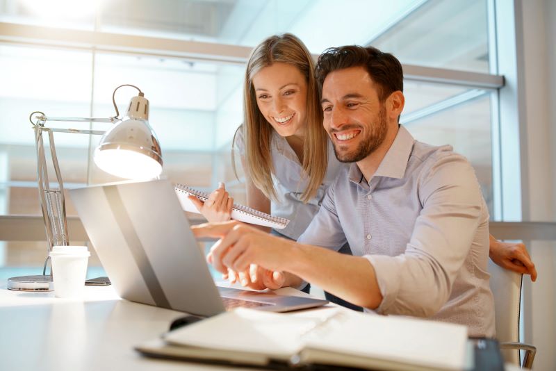 Gestão de contas​​: homem e mulher sorridentes visualizando dados na tela do computador.