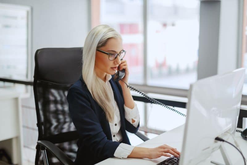 Tipos de riscos: mulher falando ao telefone e trabalhando no computador.