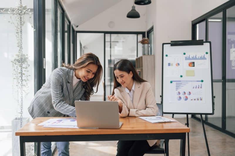 Estudo caso controle​: duas mulheres analisando informações em notebook e gráficos.