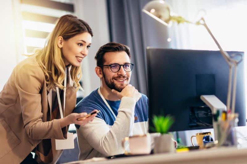 Modelo de avaliação de desempenho​: mulher e homem sorridentes olhando para tela do computador.