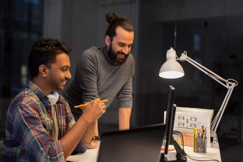 Estudos de coortes​: dois homens sorridentes olhando para monitores no escritório.
