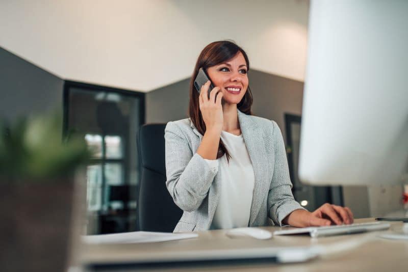 gestão de carteira​ de clientes: mulher no escritório falando com cliente por ligação no celular